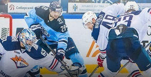 Хоккейный матч: игроки в синих и белых формах борются за шайбу у ворот. На льду виден логотип команды, а также игроки в шлемах и с клюшками. Атмосфера напряжённая и динамичная